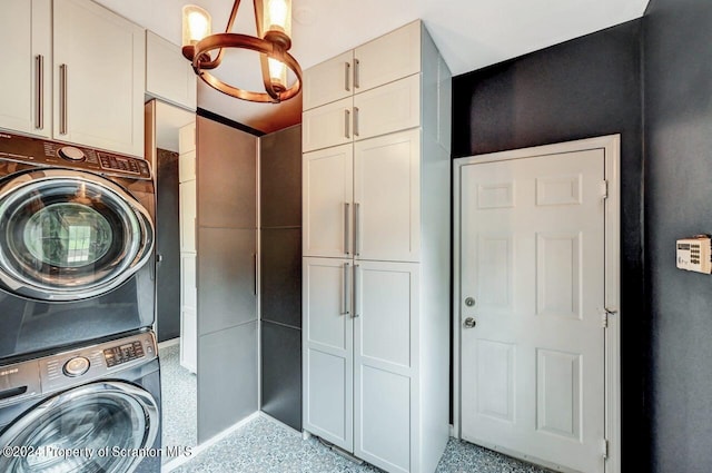 clothes washing area with cabinets, an inviting chandelier, and stacked washer / drying machine