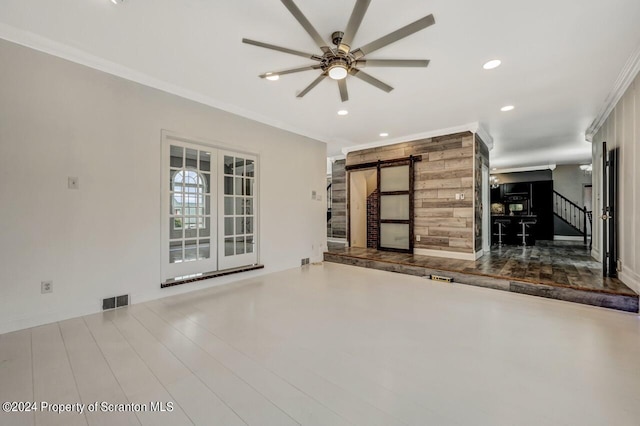 unfurnished living room with a barn door, crown molding, and ceiling fan