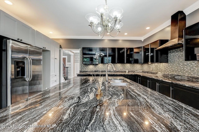 kitchen featuring sink, wall chimney range hood, dark stone countertops, stainless steel fridge, and a chandelier