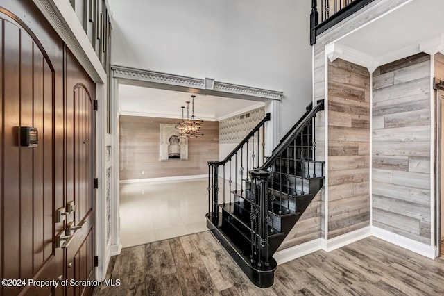 foyer entrance with a chandelier, wood-type flooring, ornamental molding, and wood walls