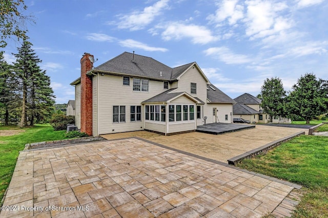 rear view of house with a deck, a lawn, a patio area, and a sunroom