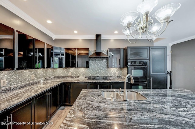 kitchen with sink, wall chimney exhaust hood, dark stone countertops, tasteful backsplash, and a notable chandelier