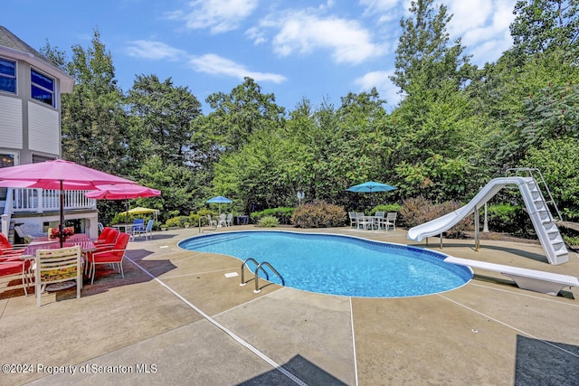 view of pool with a diving board, a water slide, and a patio