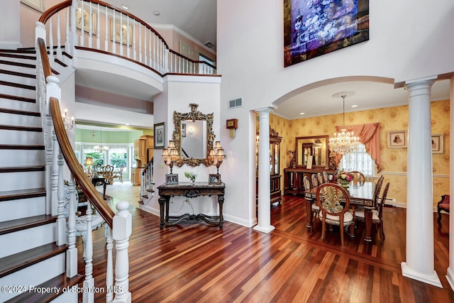 entrance foyer featuring decorative columns, hardwood / wood-style flooring, a towering ceiling, and an inviting chandelier