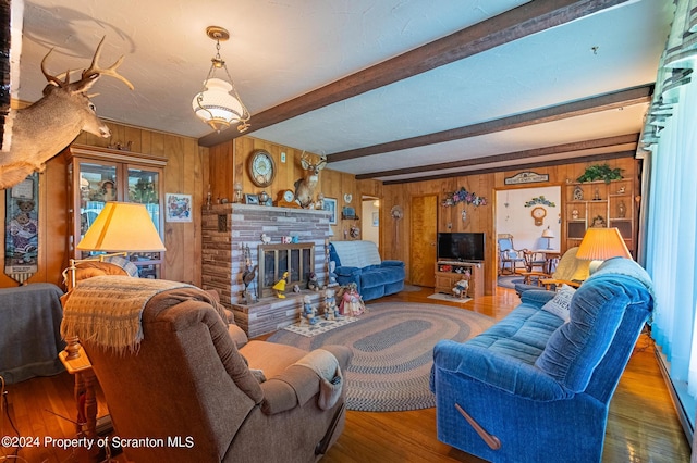 living room featuring wood walls, dark hardwood / wood-style flooring, beam ceiling, and a stone fireplace