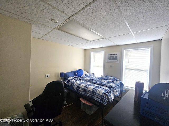 bedroom with a drop ceiling, an AC wall unit, and wood finished floors