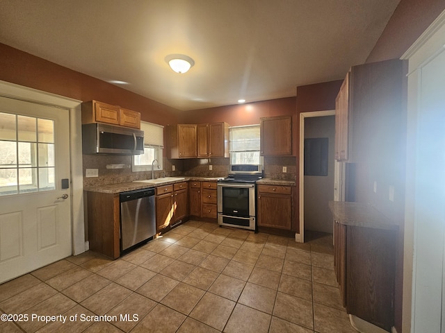 kitchen featuring tasteful backsplash, light tile patterned floors, brown cabinets, stainless steel appliances, and a sink