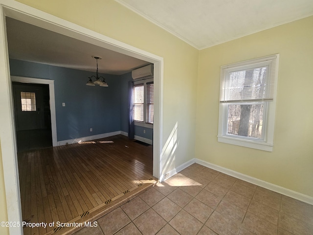 tiled spare room with a wall unit AC, a notable chandelier, and baseboards