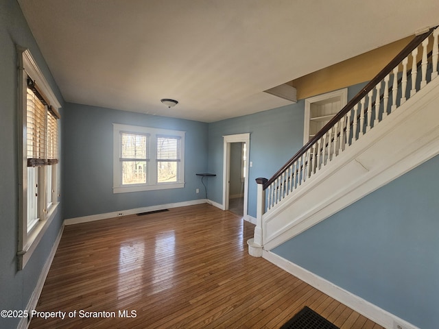 unfurnished room featuring visible vents, stairs, baseboards, and wood-type flooring