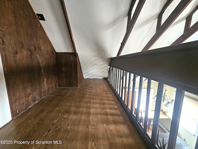 hall with vaulted ceiling, wood walls, and wood finished floors