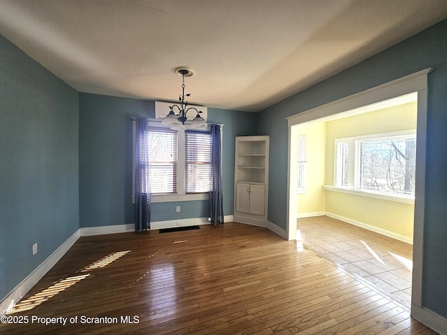 unfurnished dining area with a chandelier, baseboards, and hardwood / wood-style floors