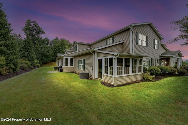 back house at dusk featuring a yard and a sunroom