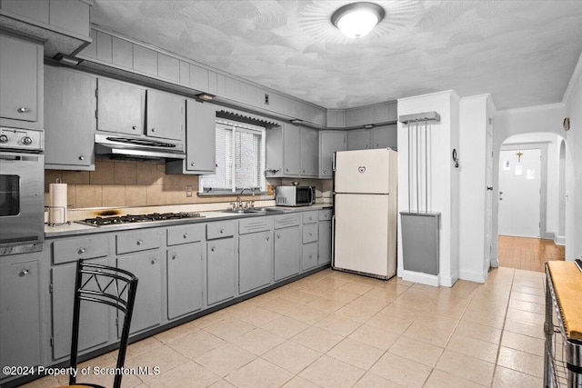 kitchen featuring wall oven, gray cabinets, white fridge, and stainless steel gas cooktop