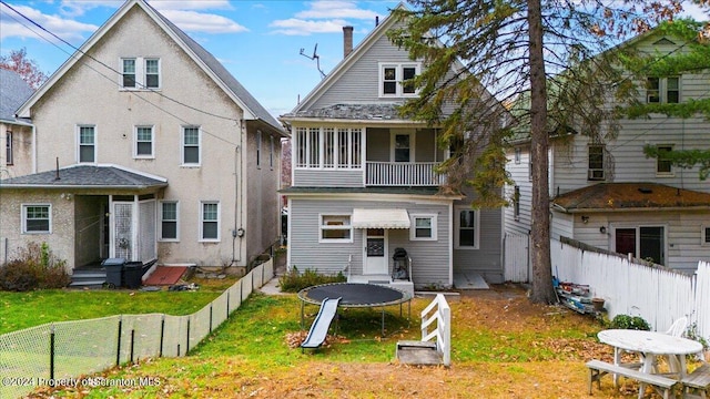 rear view of house with a lawn, a balcony, and a trampoline