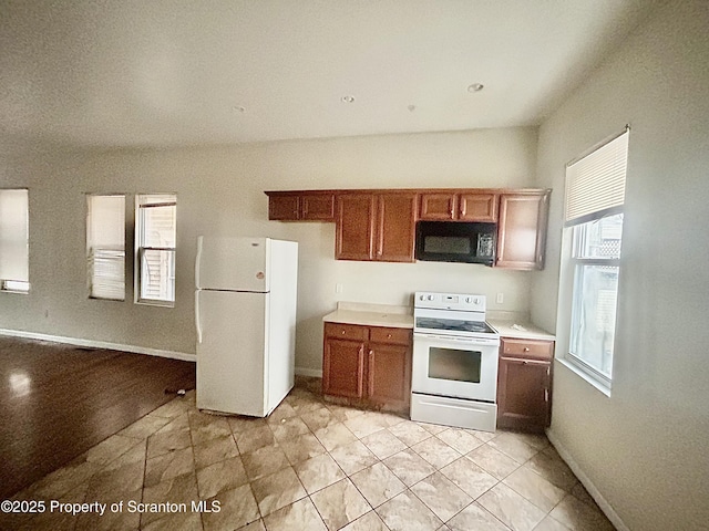 kitchen with baseboards, white appliances, brown cabinetry, and light countertops