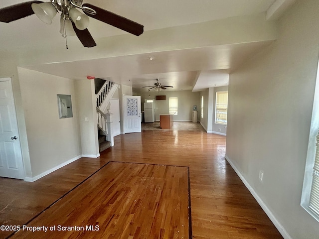 unfurnished living room with ceiling fan, baseboards, stairs, electric panel, and wood finished floors