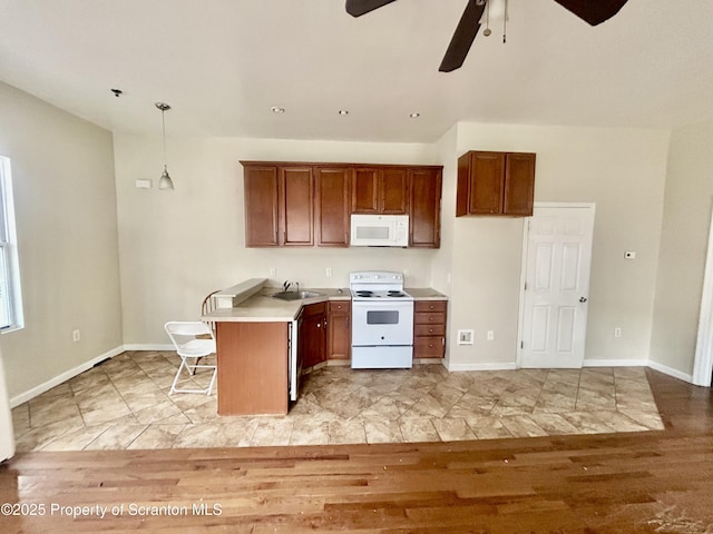 kitchen with baseboards, light countertops, brown cabinetry, white appliances, and a sink