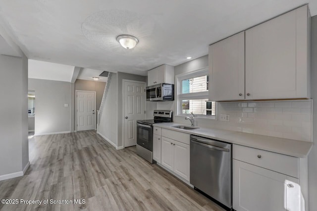 kitchen with baseboards, a sink, appliances with stainless steel finishes, and white cabinets