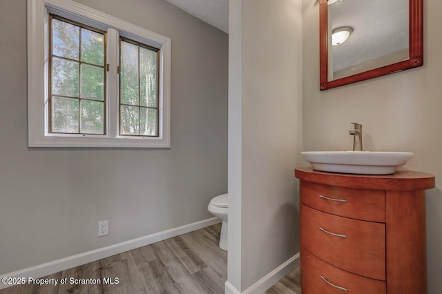 half bathroom featuring baseboards, wood finished floors, toilet, and vanity