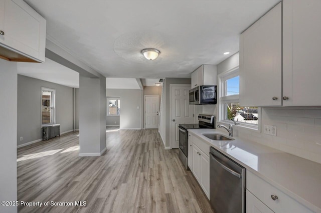kitchen featuring appliances with stainless steel finishes, a sink, light countertops, white cabinets, and a wealth of natural light