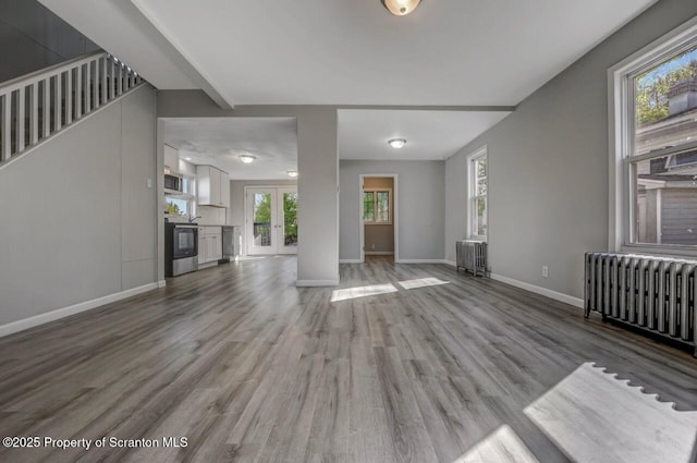 unfurnished living room featuring radiator heating unit, baseboards, and wood finished floors