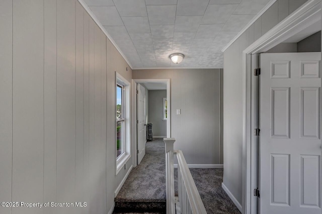 corridor with carpet flooring, wooden walls, crown molding, baseboards, and an upstairs landing