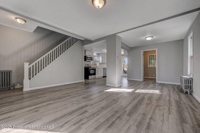 unfurnished living room with radiator heating unit, baseboards, and light wood-style floors