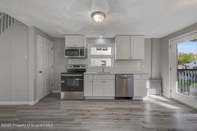 kitchen featuring stainless steel appliances, baseboards, white cabinetry, and light wood finished floors