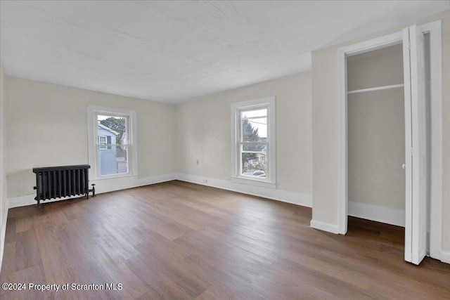 unfurnished bedroom with dark hardwood / wood-style flooring, radiator heating unit, and a closet