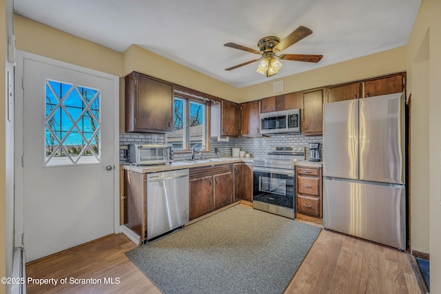 kitchen with sink, backsplash, ceiling fan, stainless steel appliances, and light wood-type flooring