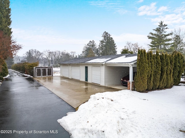 view of snowy exterior featuring a garage, an outdoor structure, and a carport