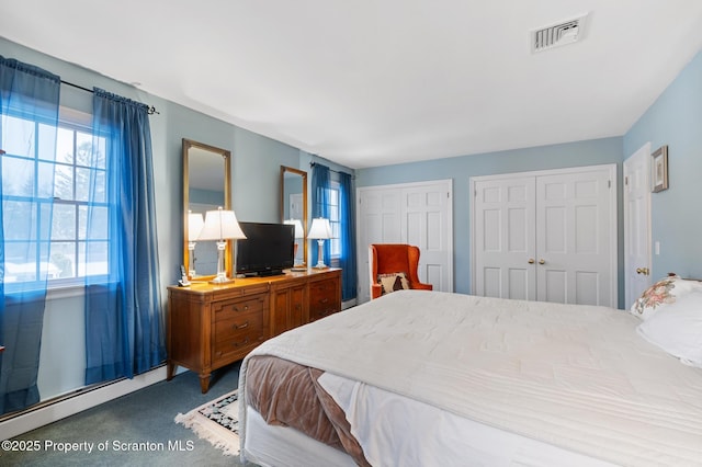 carpeted bedroom with multiple closets and a baseboard heating unit