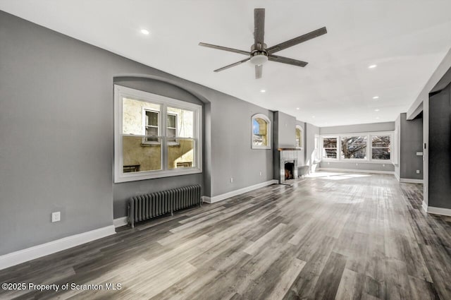 unfurnished living room with baseboards, a fireplace with raised hearth, radiator heating unit, and wood finished floors