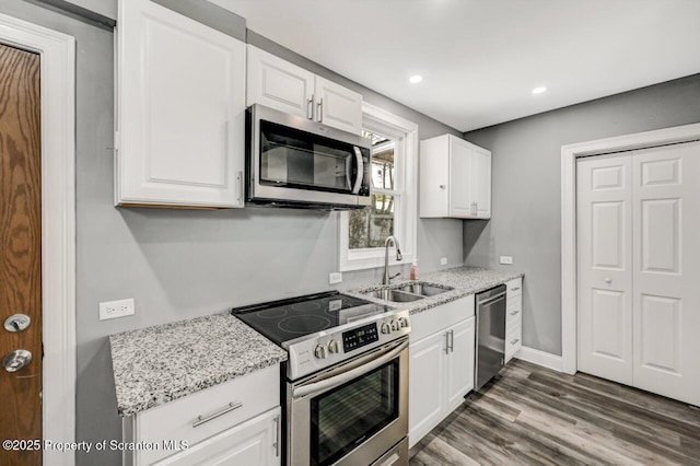 kitchen featuring light stone counters, stainless steel appliances, a sink, wood finished floors, and white cabinets