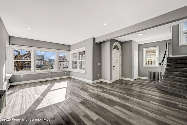 unfurnished living room with stairs, baseboards, wood finished floors, and radiator