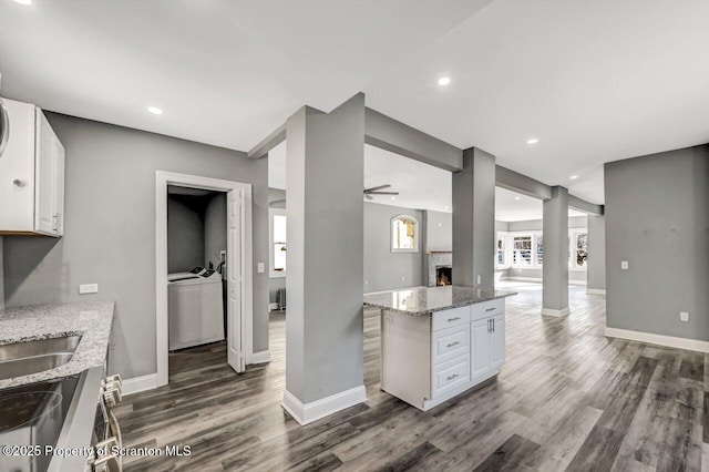 kitchen with a warm lit fireplace, baseboards, white cabinets, and dark wood-style flooring