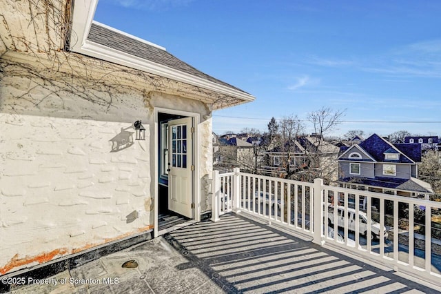 view of exterior entry with a shingled roof, a residential view, and a balcony