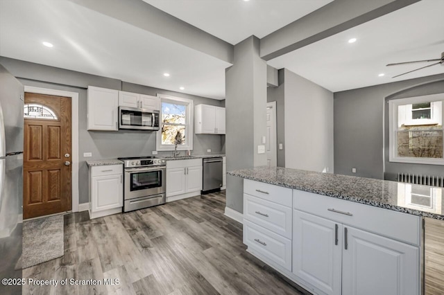 kitchen with stainless steel appliances, a sink, light stone counters, and wood finished floors