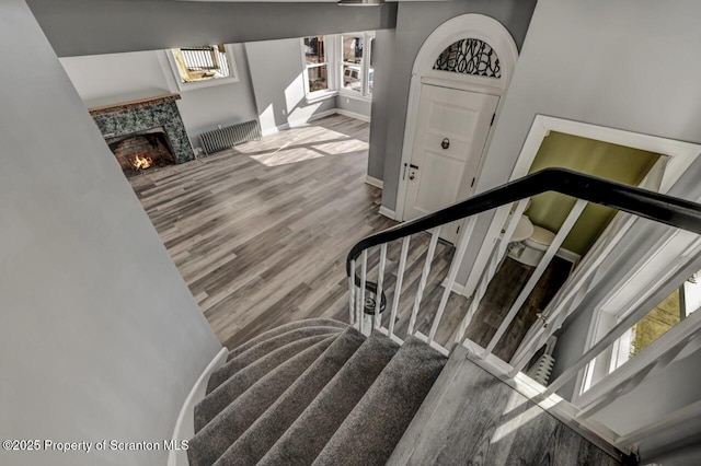 stairway featuring baseboards, a fireplace, wood finished floors, and a healthy amount of sunlight