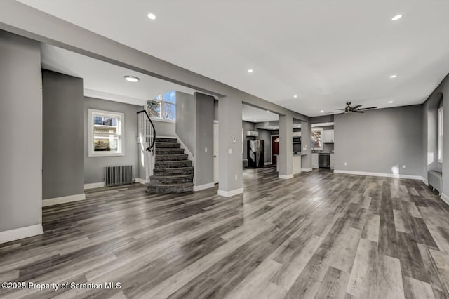 unfurnished living room featuring radiator, baseboards, stairway, and wood finished floors