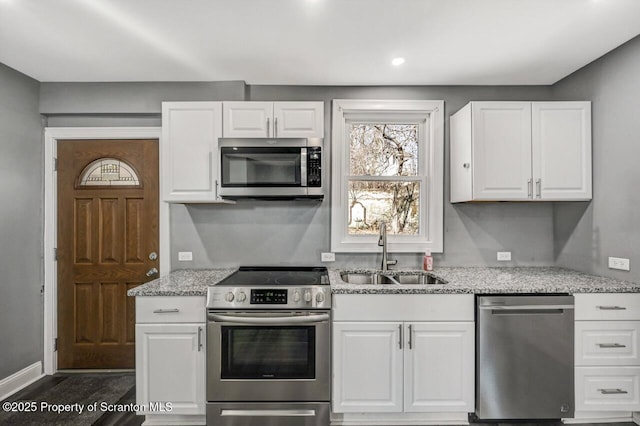 kitchen with stainless steel appliances, white cabinets, a sink, and light stone counters