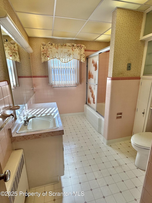 full bathroom featuring toilet, shower / bath combination with glass door, tile walls, vanity, and radiator heating unit