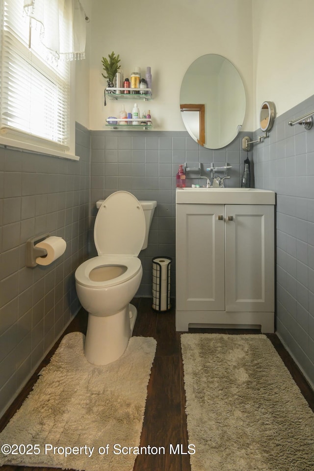 bathroom featuring vanity, wood finished floors, wainscoting, tile walls, and toilet