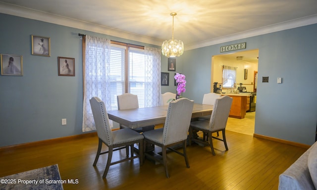 dining room featuring a chandelier, baseboards, wood finished floors, and crown molding