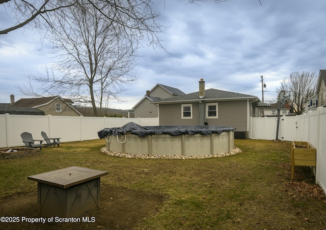 back of property featuring a fenced backyard, a fenced in pool, a chimney, and a yard