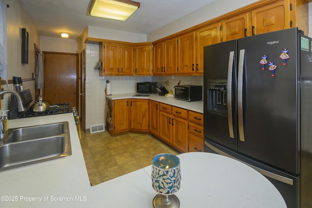 kitchen with visible vents, a sink, black appliances, light countertops, and brown cabinets