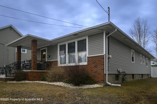 view of home's exterior with brick siding, covered porch, and a lawn