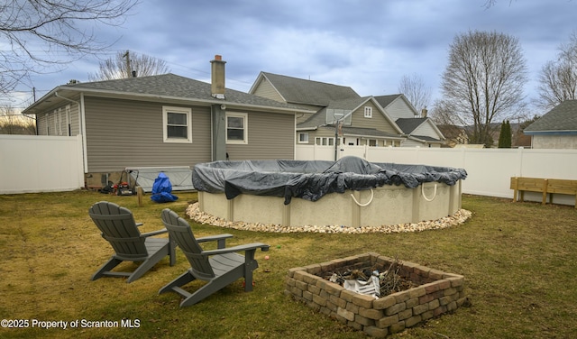 rear view of property featuring a fenced in pool, a lawn, a fenced backyard, and an outdoor fire pit