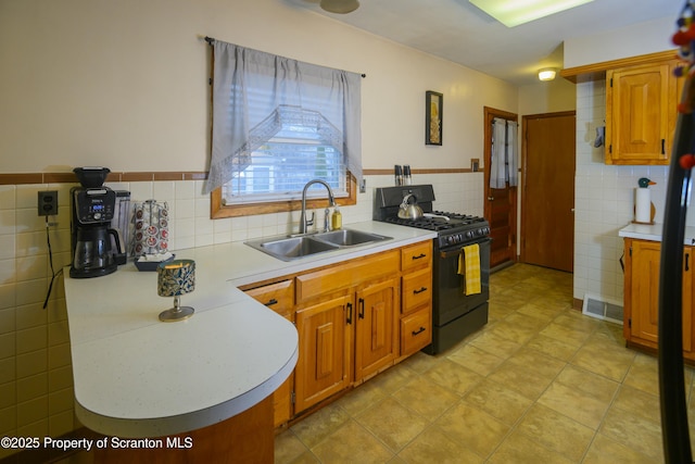 kitchen featuring black gas stove, tile walls, light countertops, and a sink