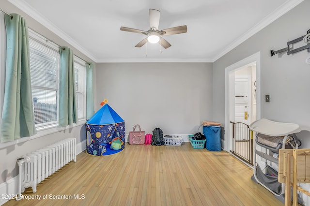 rec room with hardwood / wood-style flooring, ceiling fan, crown molding, and radiator